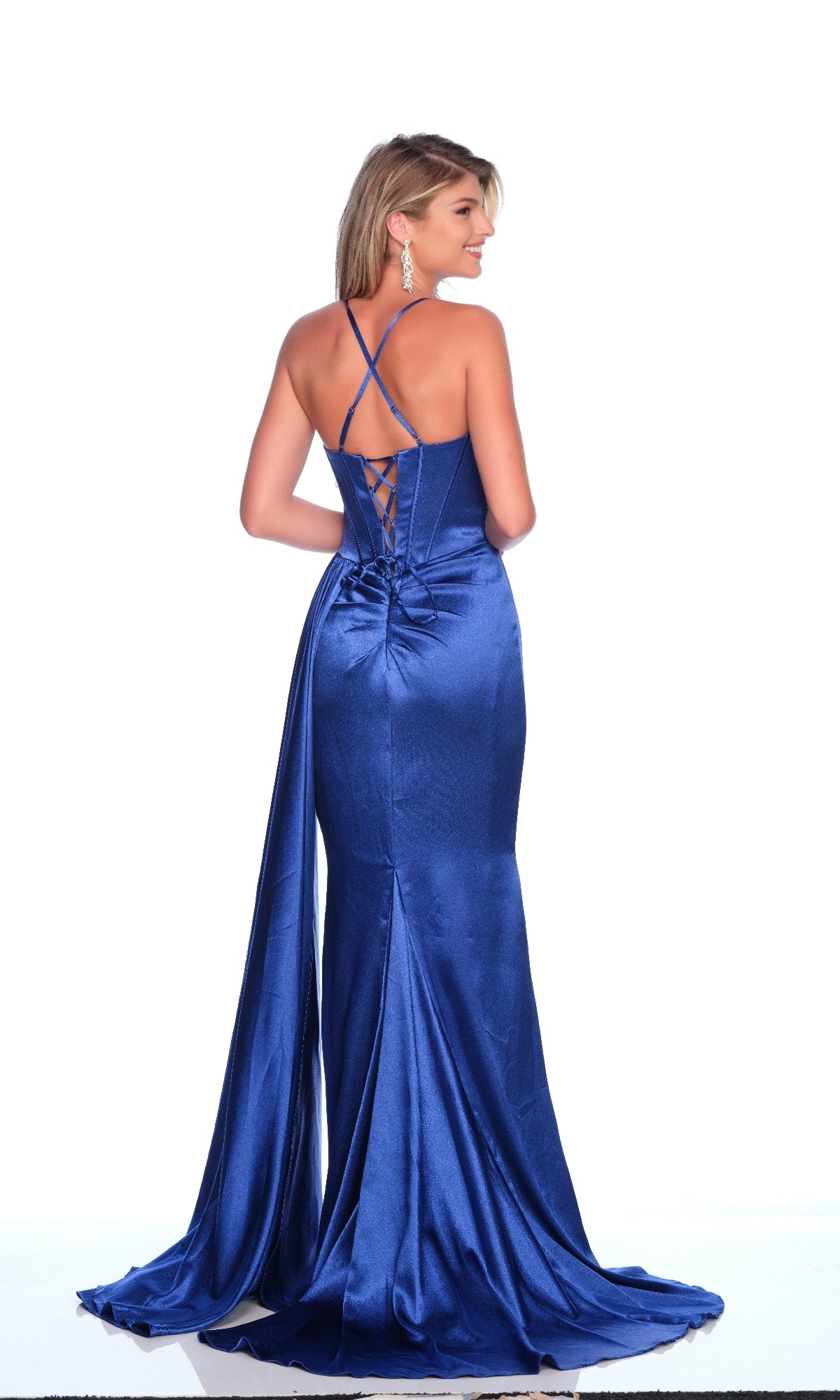 A woman stands against a white background wearing the Dave & Johnny 12217 Royal Blue Prom Dress, featuring a floor-length design, corset back, and crisscross straps.